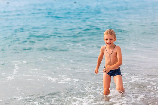 Happy active little boy having fun in the spalshes in the waves at the seaside