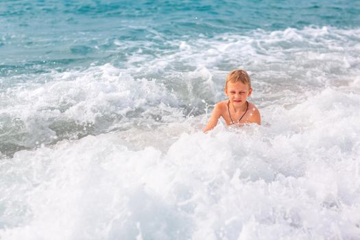 Happy active little boy having fun in the spalshes in the waves at the seaside