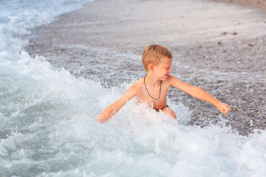 Happy active little boy having fun in the spalshes in the waves at the seaside