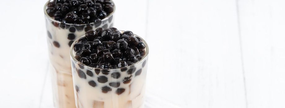 Bubble milk tea with tapioca pearl topping, famous Taiwanese drink on white wooden table background in drinking glass, close up, copy space