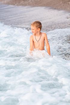 Happy active little boy having fun in the spalshes in the waves at the seaside