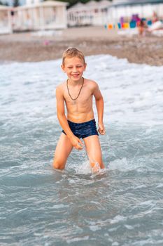 Happy active little boy having fun in the waves at the seaside