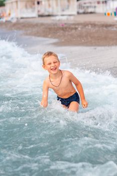Happy active little boy having fun in the waves at the seaside