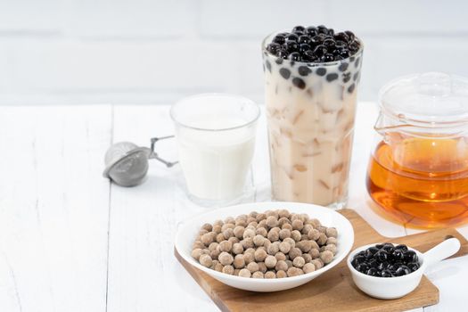 Bubble milk tea with tapioca pearl topping ingredient, famous Taiwanese drink on white wooden table background in drinking glass, close up, copy space