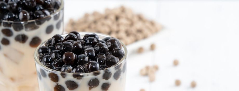 Bubble milk tea with tapioca pearl topping ingredient, famous Taiwanese drink on white wooden table background in drinking glass, close up, copy space