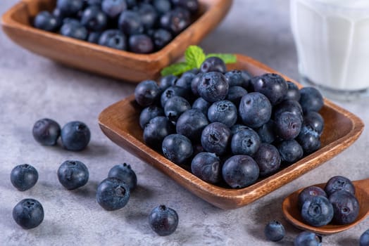 Pile of blueberry fruit in a bowl plate on a tray over gray cement concrete background, close up, healthy eating design concept.