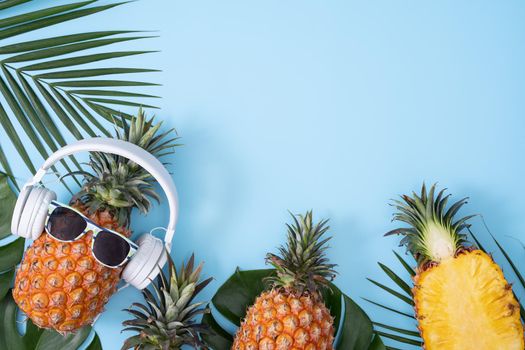 Funny pineapple wearing white headphone, concept of listening music, isolated on colored background with tropical palm leaves, top view, flat lay design.