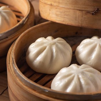 Delicious baozi, Chinese steamed meat bun is ready to eat on serving plate and steamer, close up, copy space product design concept.