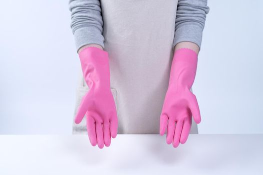 Young woman housekeeper in apron is wearing pink gloves to clean the table, concept of preventing virus infection, housekeeping service, close up.