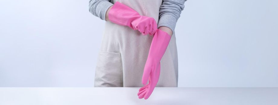 Young woman housekeeper in apron is wearing pink gloves to clean the table, concept of preventing virus infection, housekeeping service, close up.