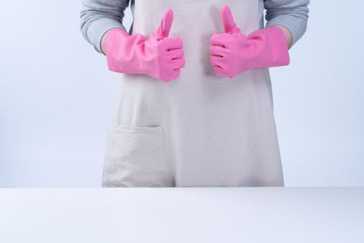 Young woman housekeeper in apron is wearing pink gloves to clean the table, concept of preventing virus infection, housekeeping service, close up.
