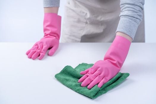 Young woman housekeeper in apron is wearing pink gloves to clean the table, concept of preventing virus infection, housekeeping service, close up.