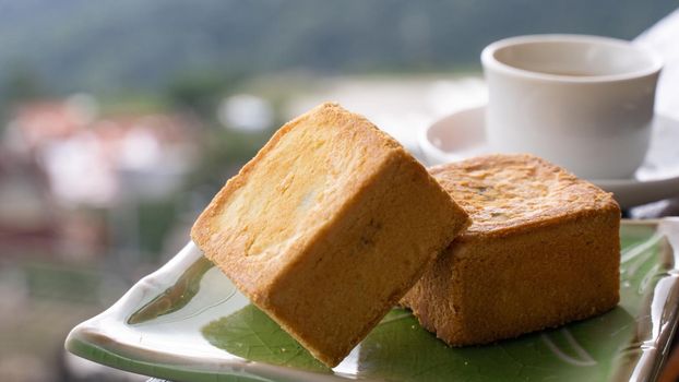 Delicious pineapple pastry in a plate for afternoon tea on wooden railing of a teahouse in Taiwan with beautiful landscape in background, close up.