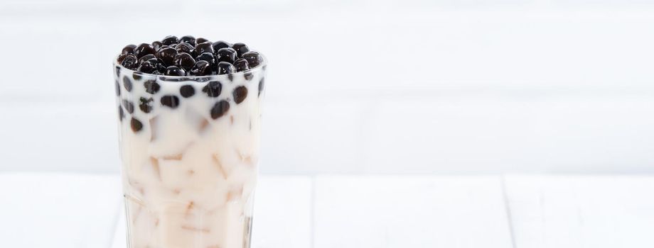 Bubble milk tea with tapioca pearl topping, famous Taiwanese drink on white wooden table background in drinking glass, close up, copy space