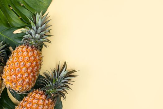 Beautiful pineapple on tropical palm monstera leaves isolated on bright pastel yellow background, top view, flat lay, overhead above summer fruit.