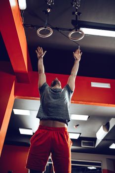 Young muscular man doing exercise on gymnast rings at the gym.