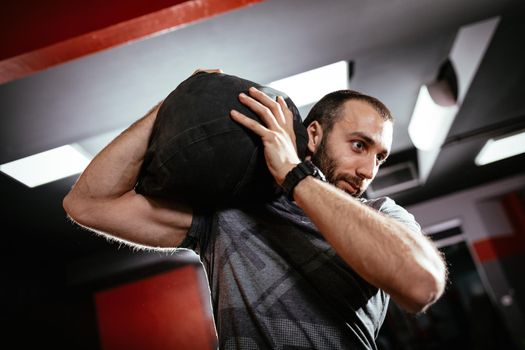 Strong man doing cross training with sandbag at the gym.