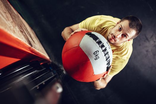 Handsome young muscular man doing exercise with wall ball at the gym. Top view. Looking at camera.