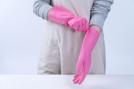 Young woman housekeeper in apron is wearing pink gloves to clean the table, concept of preventing virus infection, housekeeping service, close up.