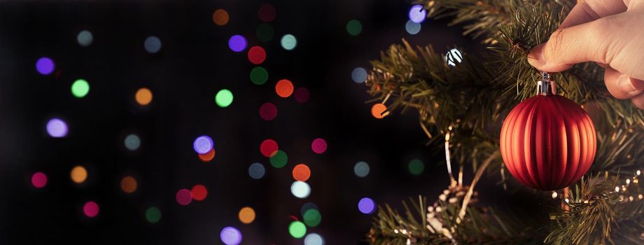 Christmas background concept- beautiful decor bauble hanging on the Christmas tree with sparkling light spot, blurry dark black background, copy space, close up.