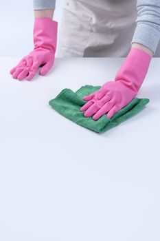 Young woman housekeeper in apron is wearing pink gloves to clean the table, concept of preventing virus infection, housekeeping service, close up.
