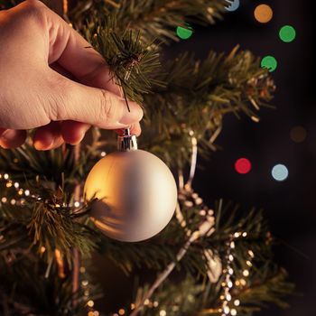 Christmas background concept- beautiful decor bauble hanging on the Christmas tree with sparkling light spot, blurry dark black background, copy space, close up.