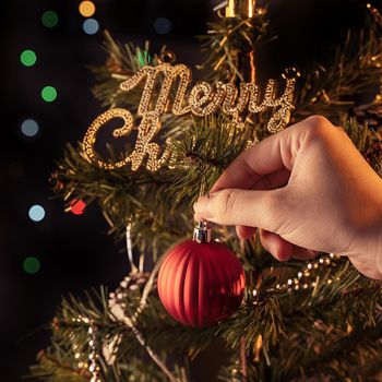 Christmas background concept- beautiful decor bauble hanging on the Christmas tree with sparkling light spot, blurry dark black background, copy space, close up.