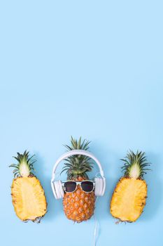 Funny pineapple wearing white headphone, concept of listening music, isolated on colored background with tropical palm leaves, top view, flat lay design.
