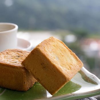 Delicious pineapple pastry in a plate for afternoon tea on wooden railing of a teahouse in Taiwan with beautiful landscape in background, close up.