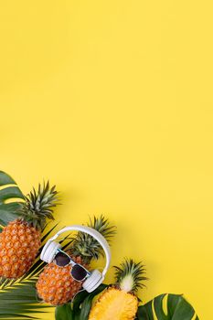 Funny pineapple wearing white headphone, listen music, isolated on yellow background with tropical palm leaves, top view, flat lay design concept.