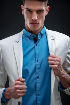 Fashion shot of a handsome young man in elegant white jacket, and beautiful turquoise shirt. Looking at camera.