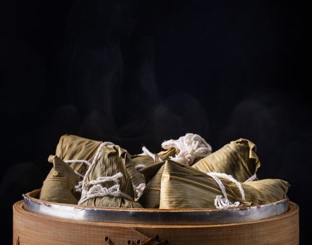 Rice dumpling, zongzi - Dragon Boat Festival, Bunch of Chinese traditional cooked food in steamer on wooden table over black background, close up, copy space