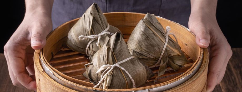 Rice dumpling, zongzi - Dragon Boat Festival, Bunch of Chinese traditional cooked food in steamer on wooden table over black background, close up, copy space