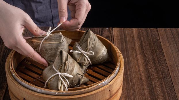 Rice dumpling, zongzi - Dragon Boat Festival, Bunch of Chinese traditional cooked food in steamer on wooden table over black background, close up, copy space