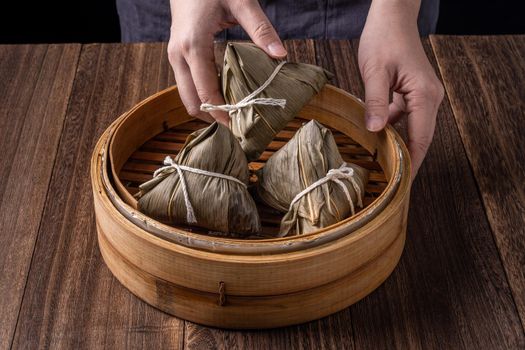 Rice dumpling, zongzi - Dragon Boat Festival, Bunch of Chinese traditional cooked food in steamer on wooden table over black background, close up, copy space
