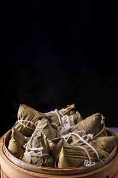 Rice dumpling, zongzi - Dragon Boat Festival, Bunch of Chinese traditional cooked food in steamer on wooden table over black background, close up, copy space