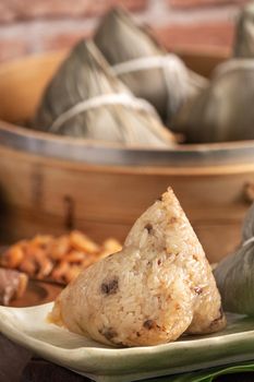 Rice dumpling - Chinese zongzi food in a steamer on wooden table with red brick wall, window background at home for Dragon Boat Festival concept, close up.