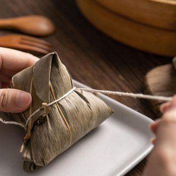 Eating zongzi - Dragon Boat Festival Rice dumpling young Asian woman eating Chinese traditional food on wooden table at home celebration, close up