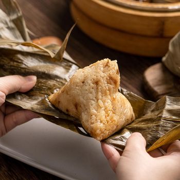 Eating zongzi - Dragon Boat Festival Rice dumpling young Asian woman eating Chinese traditional food on wooden table at home celebration, close up