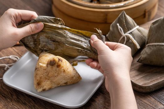 Eating zongzi - Dragon Boat Festival Rice dumpling young Asian woman eating Chinese traditional food on wooden table at home celebration, close up