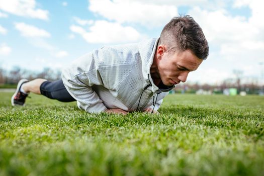 Young man athlete doing push ups and doing exercises on the green grass, during the spring training outside in.