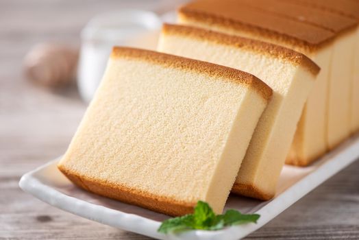 Castella - Delicious Japanese sliced sponge cake food on white plate over rustic wooden table, close up, healthy eating, copy space design.