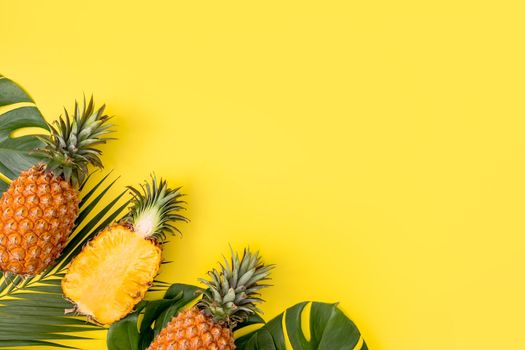 Beautiful pineapple on tropical palm monstera leaves isolated on bright pastel yellow background, top view, flat lay, overhead above summer fruit.