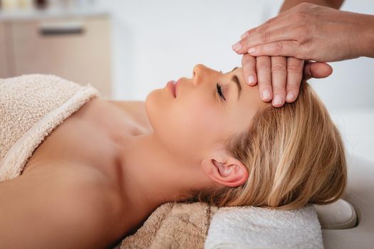 Close-up of a beautiful healthy young woman enjoying relaxing facial massage at beauty salon. 