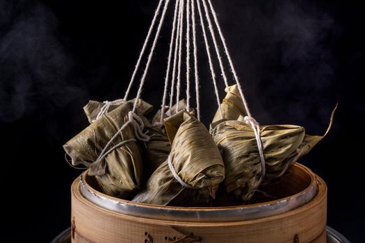 Rice dumpling, zongzi - Dragon Boat Festival, Bunch of Chinese traditional cooked food in steamer on wooden table over black background, close up, copy space