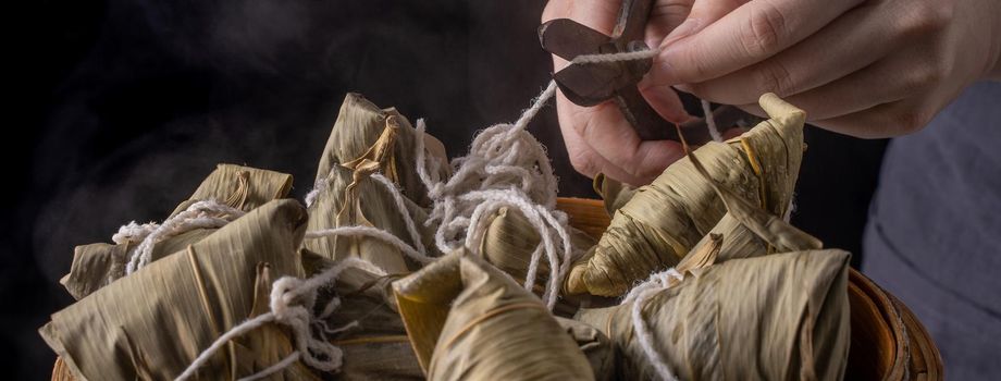 Rice dumpling, zongzi - Dragon Boat Festival, Bunch of Chinese traditional cooked food in steamer on wooden table over black background, close up, copy space