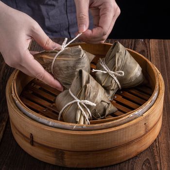 Rice dumpling, zongzi - Dragon Boat Festival, Bunch of Chinese traditional cooked food in steamer on wooden table over black background, close up, copy space