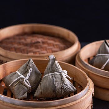 Rice dumpling, zongzi - Dragon Boat Festival, Bunch of Chinese traditional cooked food in steamer on wooden table over black background, close up, copy space