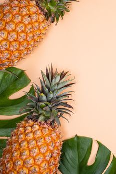 Beautiful pineapple on tropical palm monstera leaves isolated on bright pastel orange yellow background, top view, flat lay, overhead above summer fruit.