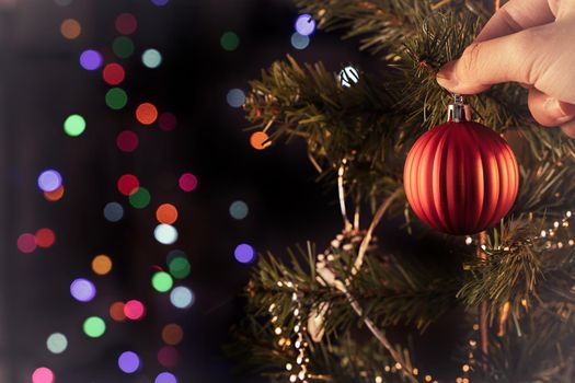 Christmas background concept- beautiful decor bauble hanging on the Christmas tree with sparkling light spot, blurry dark black background, copy space, close up.
